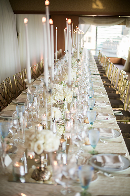 A long table with white florals and tall tapers in crystal candelabras.