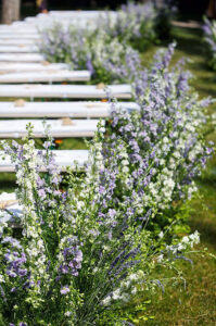 outdoor wedding ceremony with white benches and flower lined aisle