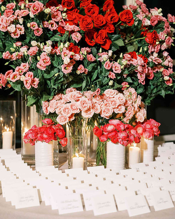 vases filled with dolorful red roses and pink lisianthus on a wedding escort card table