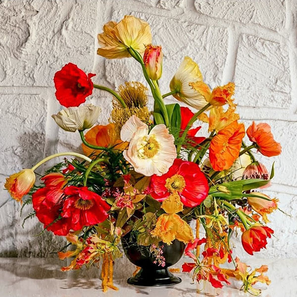 bright and colorful arrangement of red orange and yellow poppies with gloriosa lilies tulips and amaranth in a metal copper bowl rust wedding