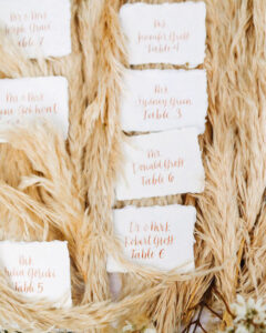 escort cards on a bed of pampas grass for a boho themed wedding