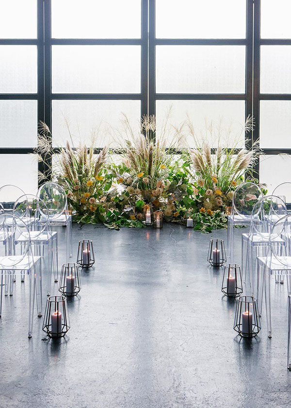 urban garden wedding ceremony decor in industrial loft candle hurricane lined aisle and floral installation with pampas grass