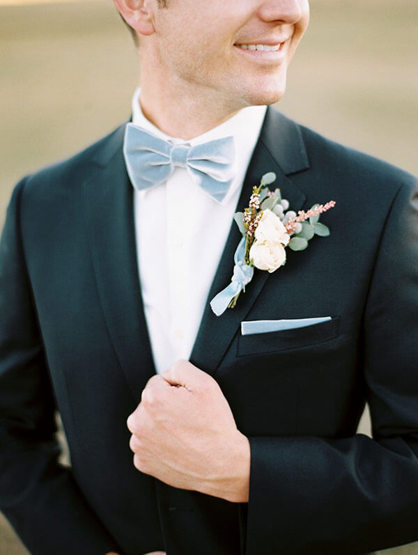 groom in gray-blue velvet bow tie, pocket square, and ribbon-wrapped boutonniére