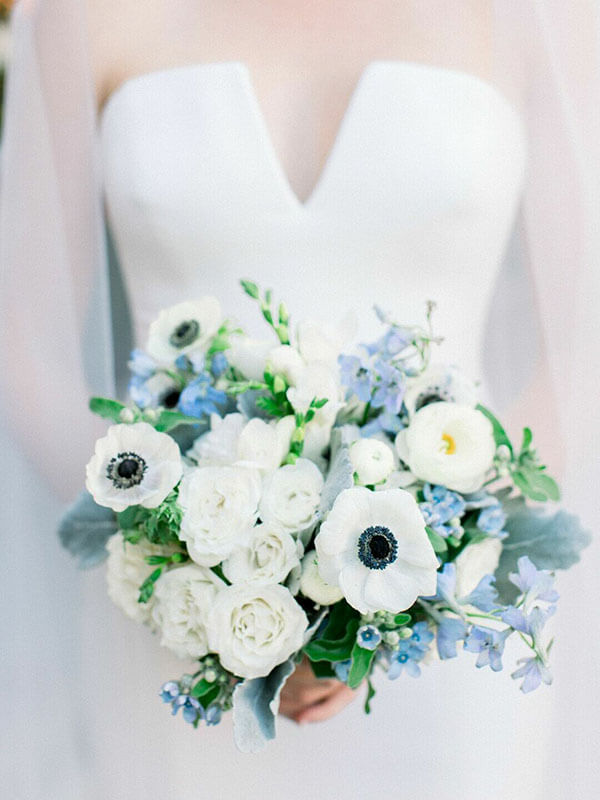bride holding white anemone bouquet with hints of light blue thanks to delphinium and forget-me-nots